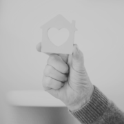 Black and white image of a person holding a house figure with a heart cut out in the middle