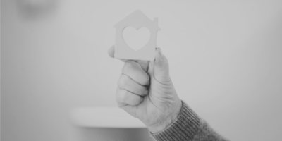 Black and white image of a person holding a house figure with a heart cut out in the middle