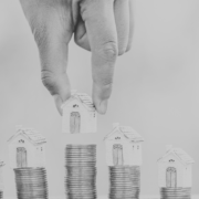 Black and white image of house figures placed on top of stacks of coins