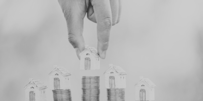 Black and white image of house figures placed on top of stacks of coins
