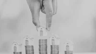 Black and white image of house figures placed on top of stacks of coins