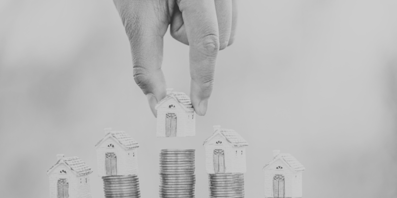 Black and white image of house figures placed on top of stacks of coins