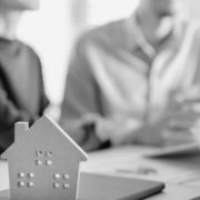 Two people talking to another person other a desk with a cut out house.