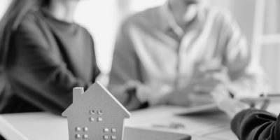 Two people talking to another person other a desk with a cut out house.