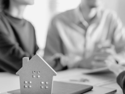Two people talking to another person other a desk with a cut out house.