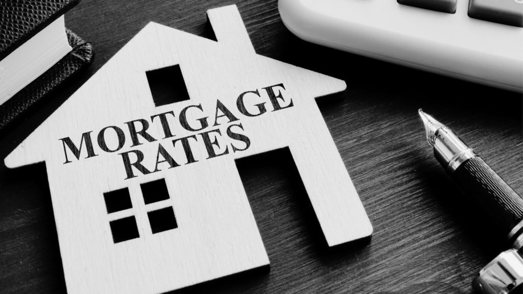 Mortgage Rates Text over cut out wooden house with pen to the right of the image