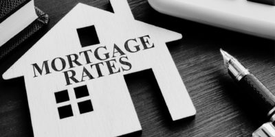 Mortgage Rates Text over cut out wooden house with pen to the right of the image