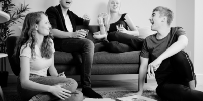 Black and white image of shared living space and 4 people with 2 sitting on the coach.
