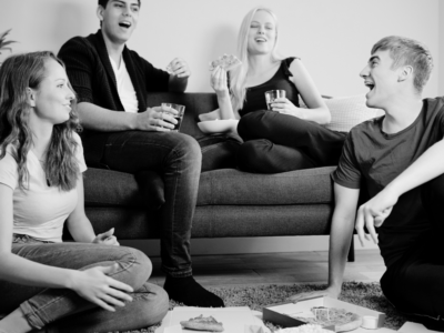 Black and white image of shared living space and 4 people with 2 sitting on the coach.