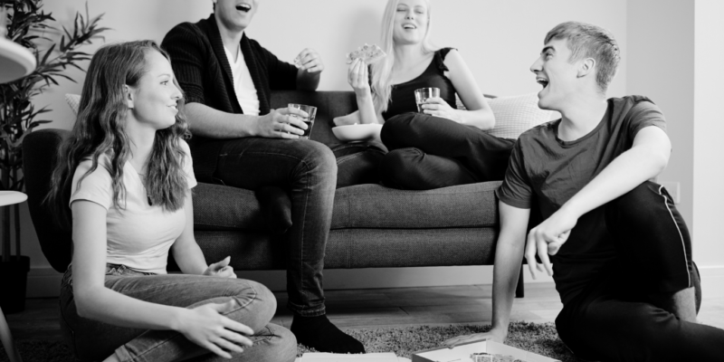 Black and white image of shared living space and 4 people with 2 sitting on the coach.