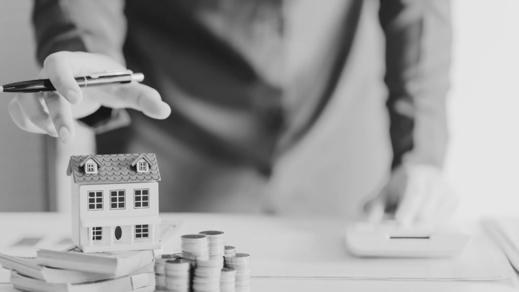 Man with house model on table and stack of coins and paperwork