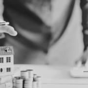 Man with house model on table and stack of coins and paperwork