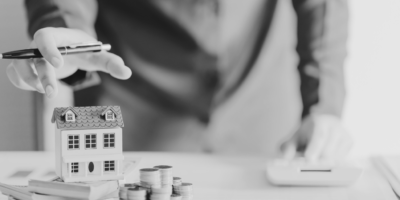 Man with house model on table and stack of coins and paperwork