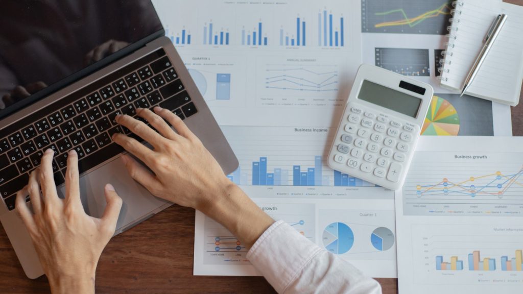 Picture with laptop and person typing with files and calculator in background