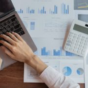 Picture with laptop and person typing with files and calculator in background