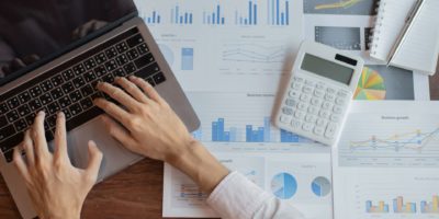 Picture with laptop and person typing with files and calculator in background