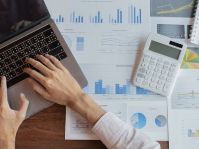 Picture with laptop and person typing with files and calculator in background