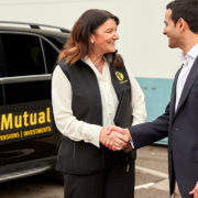 Woman shaking mans hand with van in background.