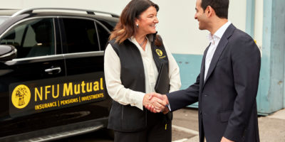 Woman shaking mans hand with van in background.