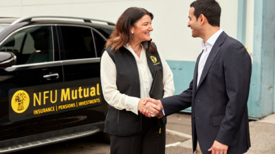 Woman shaking mans hand with van in background.