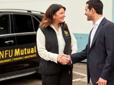 Woman shaking mans hand with van in background.